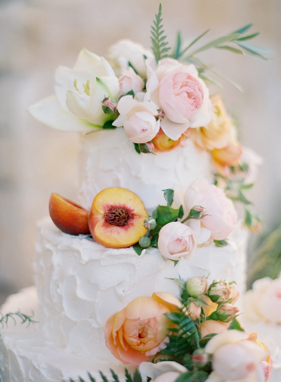 A white wedding cake with flowers and peaches. 